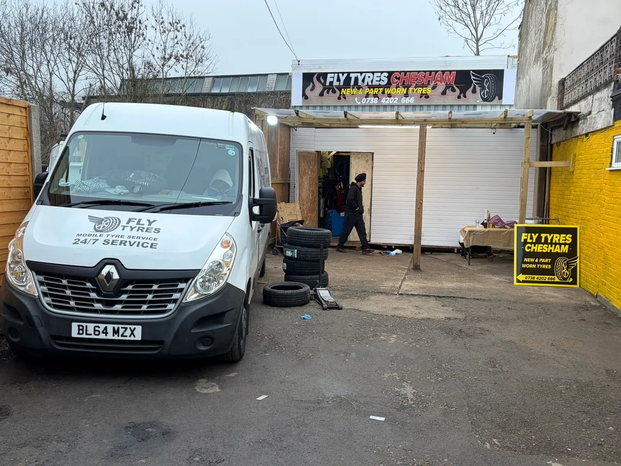 The Fly Tyres van parked outside the Fly Tyres Chesham unit, with the shutter open and tyres stacked in the yard.