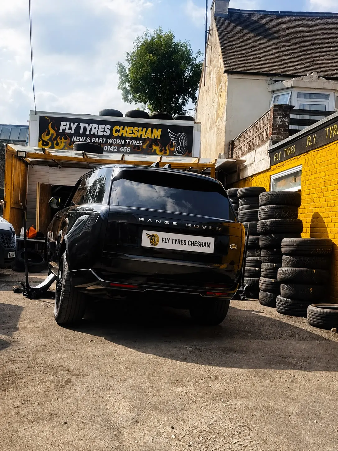 A black Range Rover parked in front of the Fly Tyres Chesham unit, with stacks of tyres against the wall beside it.