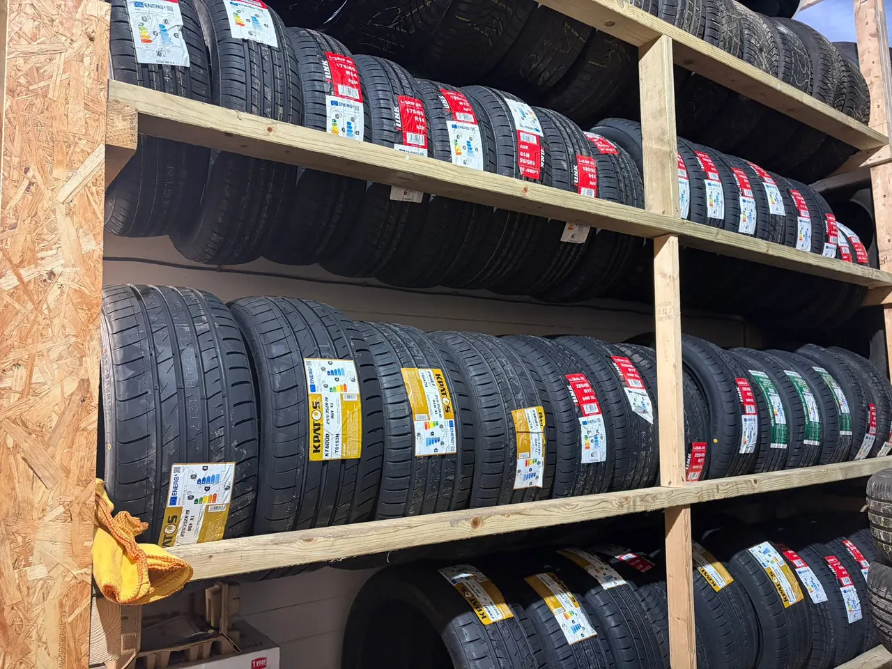 Racks of new tyres stacked several rows high inside the Fly Tyres unit, each carrying its manufacturer label.
